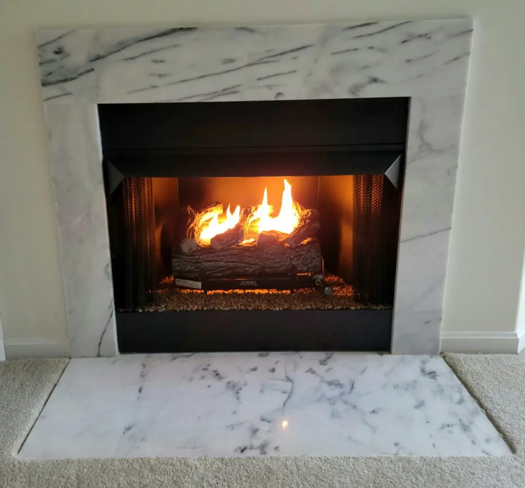 A fireplace with a log burning inside with marble covering